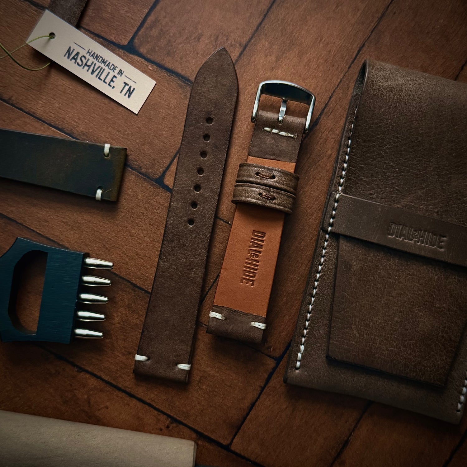 Brown leather watch strap and wallet on a wooden surface with 'Dial & hide' branding.