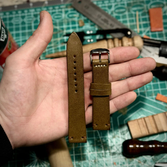 olive green leather watch strap held in a hand with tools in the background