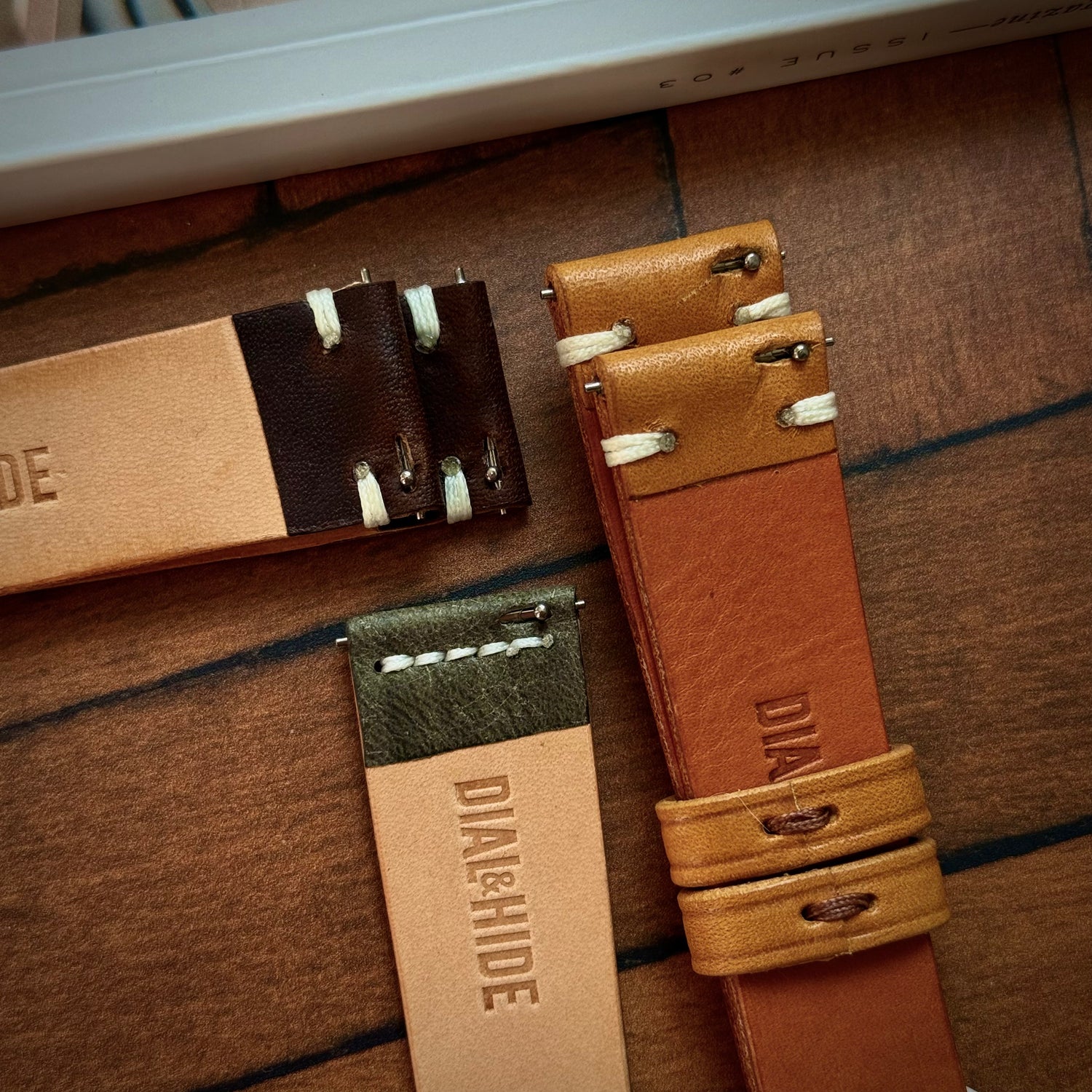 Three leather watch straps with quick release spring bars on a wooden surface with 'Dial & Hide' branding.
