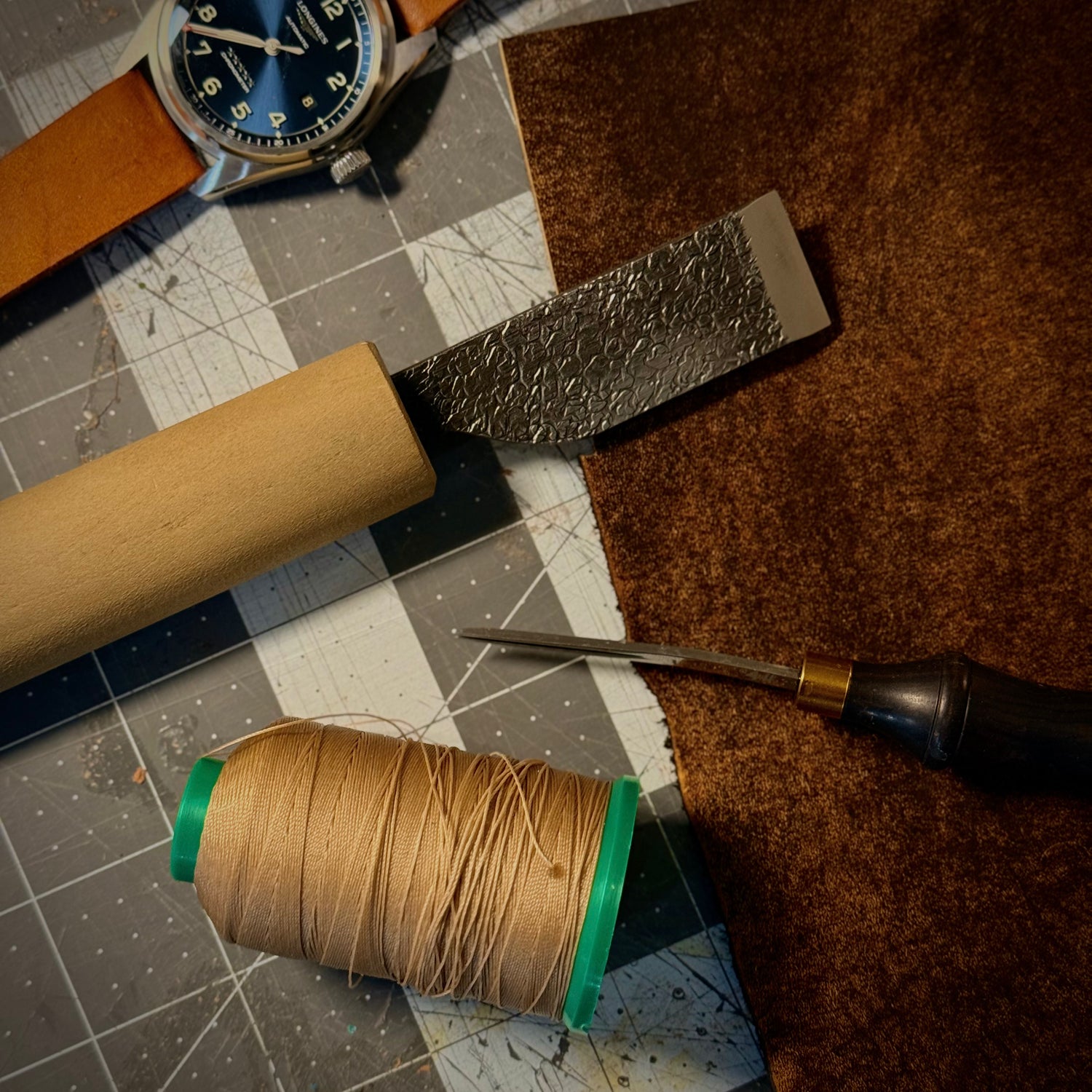 Spool of thread, leather tool, and watch on a checkered surface