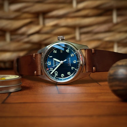 Watch with a blue face and brown leather strap on a wooden surface